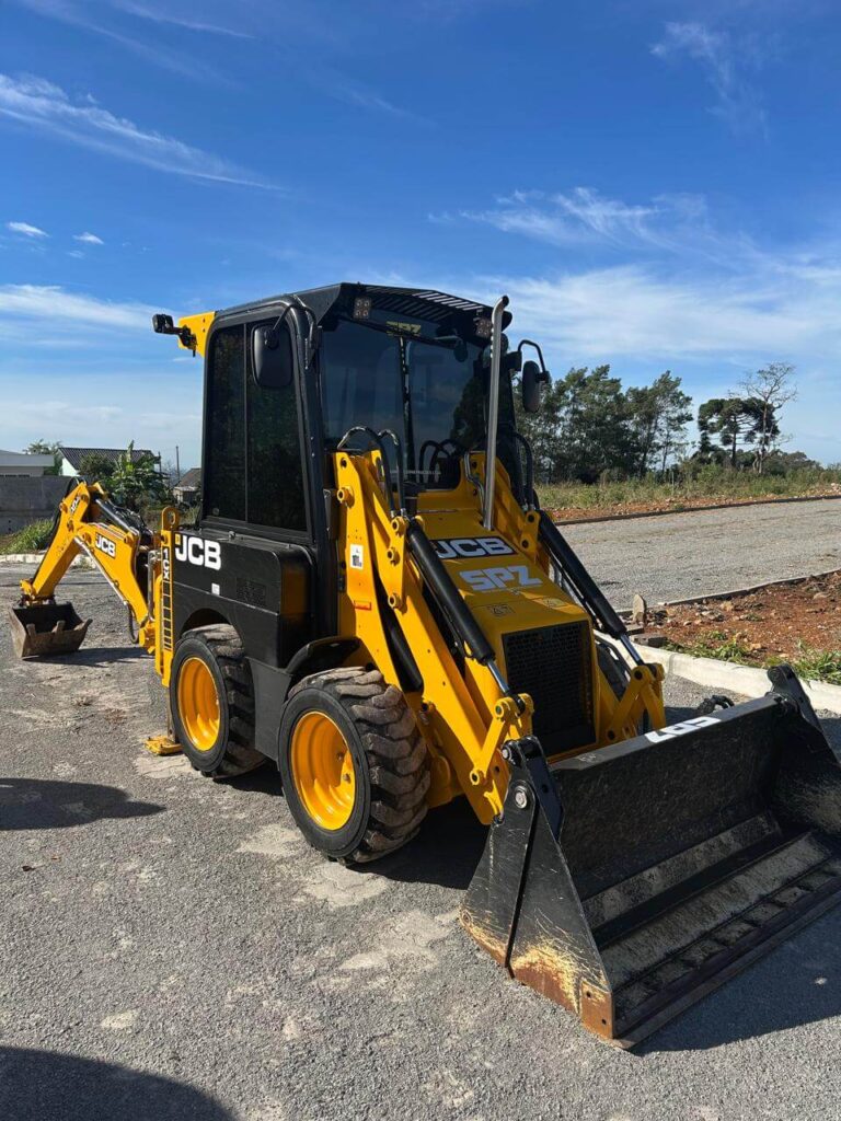 Retroescavadeira JCB amarela estacionada em área pavimentada, com céu azul ao fundo.