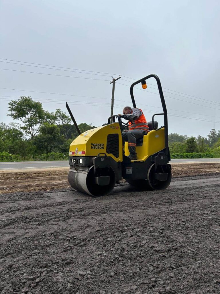 Operador utilizando rolo compactador Wacker Neuson em obra de pavimentação, compactando o solo.